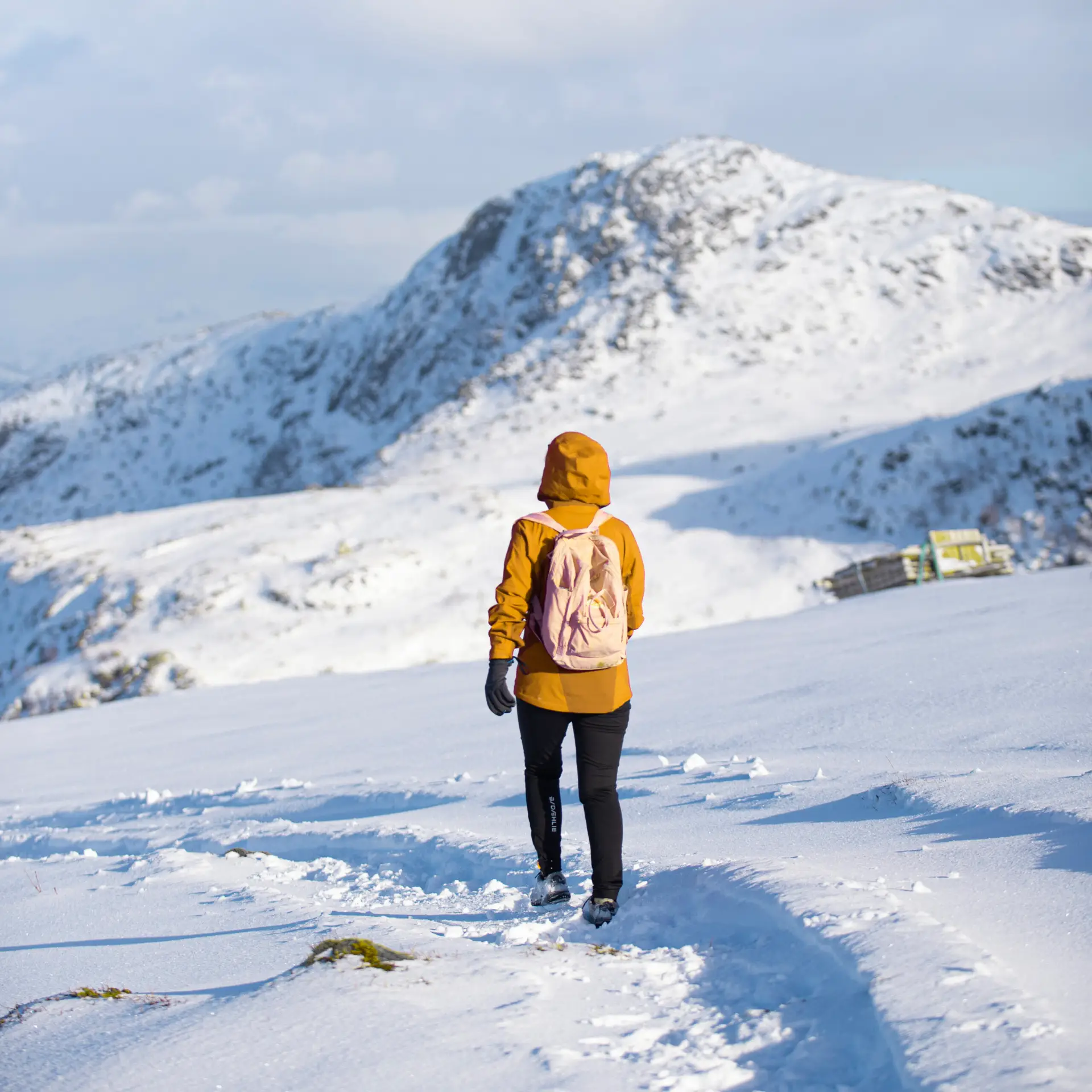 A girl in yellow jacket hiking on a snowy, white and blue mountain on a beautiful day